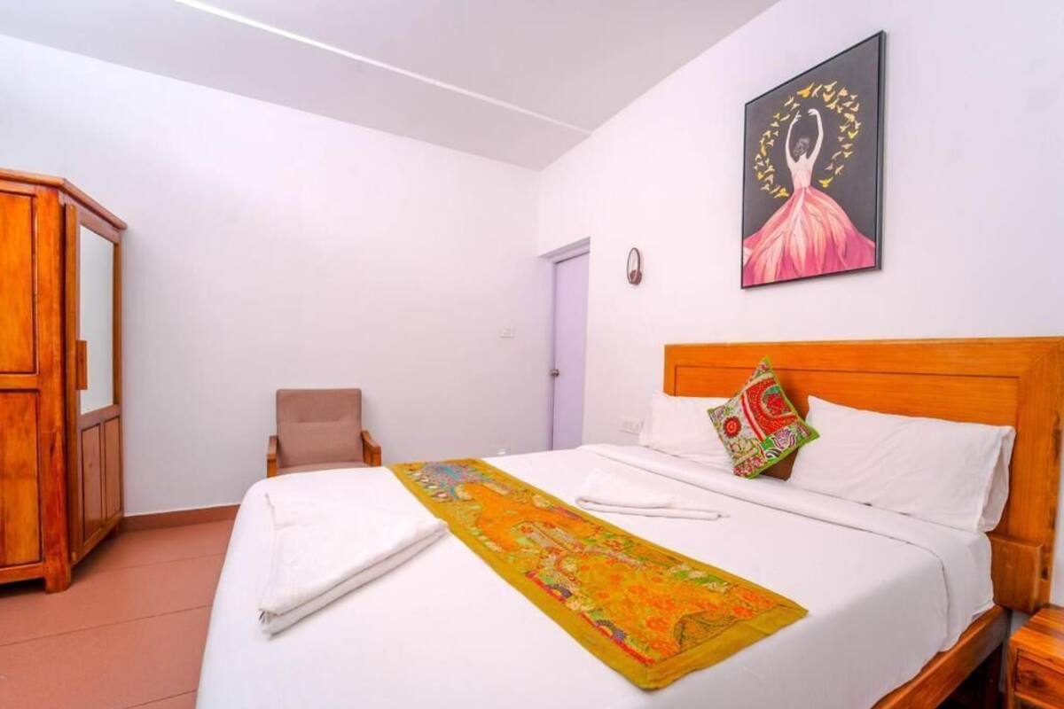 A hotel room with a bed, a wooden wardrobe, a chair, a painting on the wall, and a door.