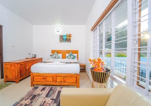 A bedroom with a wooden bed, a wooden dresser, a bedside table, a chair, and a balcony with a view. - Silent Retreat Ooty by VOYE HOMES (Ooty)
