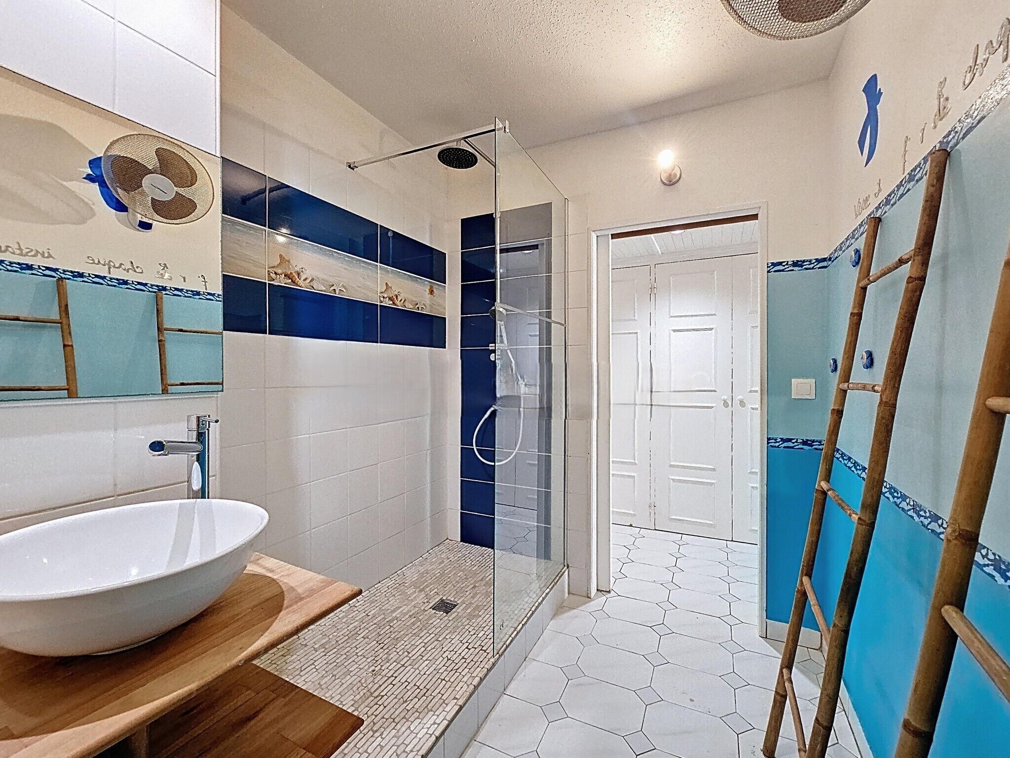 Un baño con lavamanos blanco, cabina de ducha con paredes de vidrio y escalera de madera.