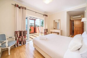 A bedroom with a bed, a chair, a vanity, and a sliding door to a balcony. - Sunlit Villa Terraces and Pool in Vilamoura by HostWise (Quarteira)