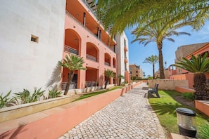 A building with a red facade, multiple balconies, and a paved pathway with palm trees. - Sunlit Villa Terraces and Pool in Vilamoura by HostWise (Quarteira)
