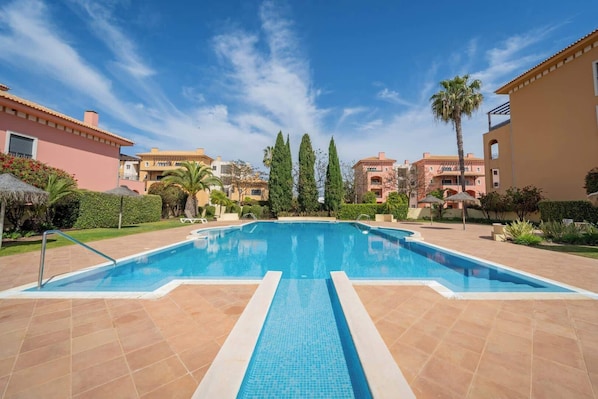 A swimming pool with a tiled deck, surrounded by buildings and greenery. - Sunlit Villa Terraces and Pool in Vilamoura by HostWise (Quarteira)