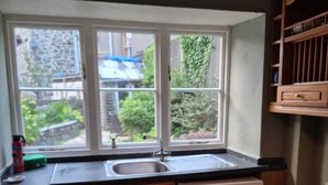Eine kleine Küche mit Holzschränken, einer integrierten Waschmaschine, einem Spülbecken und einem Fenster mit Blick auf einen Garten.