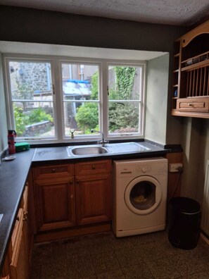 Eine kleine Küche mit Holzschränken, einer integrierten Waschmaschine, einem Spülbecken und einem Fenster mit Blick auf einen Garten.