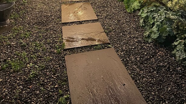 Ein gepflasterter Weg führt zu einer kleinen Außenbereich-Sitzgelegenheit mit Lichterketten darüber.
