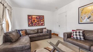 A living room with two leather sofas, a glass coffee table, and a large abstract painting on the wall. - Beautiful 3 Bedroom Flat in Fulham (London)