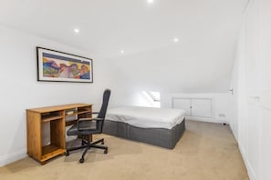 Une chambre à coucher avec un lit, un bureau, une chaise et un tableau accroché au mur.