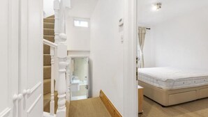 A bedroom with a bed, a window with curtains, a staircase, and a bathroom visible through an open door. - Beautiful 3 Bedroom Flat in Fulham (London)