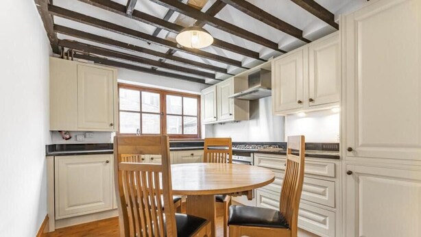 A kitchen with wooden chairs, white cabinets, a round table, and exposed wooden beams on the ceiling. - Beautiful 3 Bedroom Flat in Fulham (London)