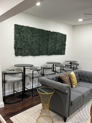 Ein modernes Interieur mit einem grauen Sofa, mehreren runden Tischen und einem Wandbehang in Grün.