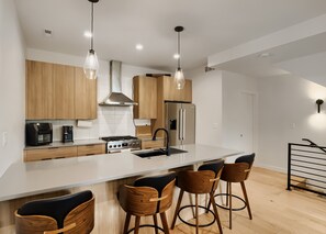 A modern kitchen with wooden cabinets, stainless steel appliances, and a central island with bar stools. - Designer Rooftop Home on Tennyson (Denver)