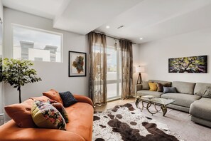 A modern living room with a sofa, a glass coffee table, and a cowhide rug. - Designer Rooftop Home on Tennyson (Denver)