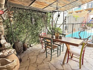 Eine Terrassensitzgelegenheit im Freien mit Holztisch und -stühlen, umgeben von Grünpflanzen und Blick auf einen Swimmingpool.