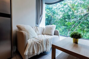 A modern living room with a sofa, a coffee table, and a view of trees through a window. - The best vacation at Kamala Beach. Clean, friendly, and quiet 709 (Tambon Kamala)