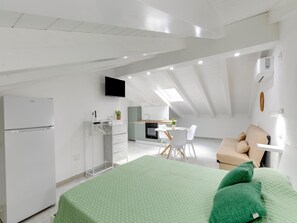 A modern loft bedroom with a green quilted bedspread, a kitchenette, a dining area, and a TV mounted on the wall. - Attic Studio, With air Conditioning (Castelsardo)
