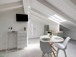 A modern kitchen with a skylight, white cabinets, and a dining area with two chairs and a table. - Attic Studio, With air Conditioning (Castelsardo)