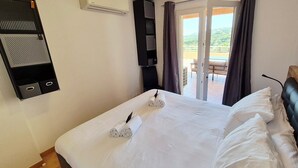 Ein Hotelzimmer mit Bett, Schreibtisch, Stuhl und Balkon mit Blick sowie einer Klimaanlage.