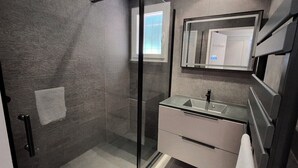 Ein modernes Badezimmer mit Duschkabine aus Glas, einem Waschbecken mit Spiegel darüber und einem Handtuchhalter.