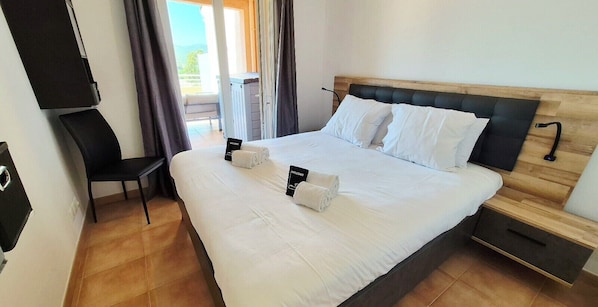 A neatly made bed with white linens and pillows, a wooden headboard, a bedside table with a lamp, and a chair.
