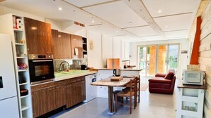 A modern kitchen with built-in appliances, a dining area with a table and chairs, and a red sofa in a spacious living area. - Completely renovated house with terrace and garden (Maisons-Alfort)