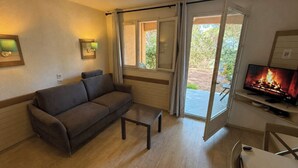 Un salon comprenant un canapé, une table basse, un téléviseur et une porte-fenêtre coulissante donnant sur un espace extérieur.