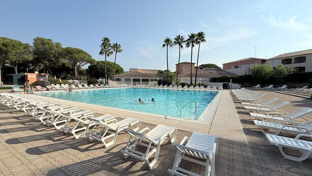 Une piscine entourée de chaises longues, de palmiers et de bâtiments en arrière-plan.