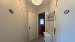 Un corridoio stretto con carta da parati decorata, un tavolo consolle bianco e una sedia rossa sullo sfondo.