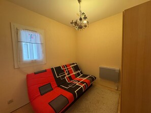 Una habitación pequeña con un sofá rojo y negro, una ventana con cortina, un radiador y un armario de madera.