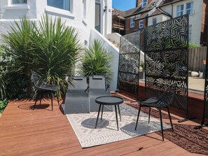Un patio con una mesa y sillas, rodeado de plantas y una valla decorativa.