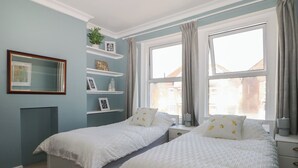 Ein Schlafzimmer mit zwei Betten, einem Fenster mit Vorhängen, einem Regal mit Dekoration und einem gemusterten Teppich.