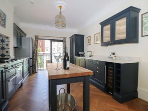 A modern kitchen with dark cabinetry, a wooden table, and a view to the outside. - East Cliff Gardens (Folkestone)