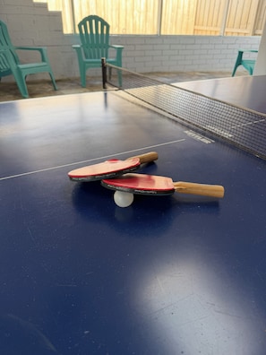 A ping pong table with two paddles and a ball, surrounded by green chairs.