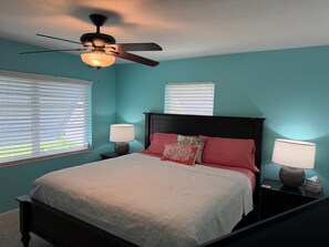 A bedroom with a bed, two bedside tables, a ceiling fan, and windows with blinds.