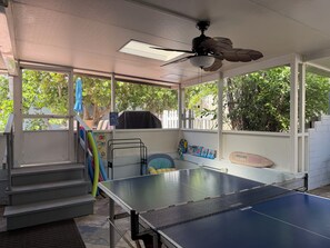 A covered outdoor area with a ping pong table, a ceiling fan, and a sign reading 'BEACH HOUSE.' - Charming 3/2 house in Jensen Beach with pool and minutes away from downtown (Jensen Beach)