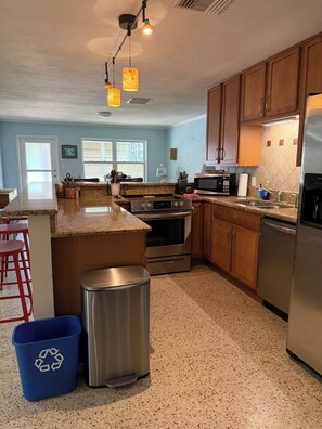 A kitchen with granite countertops, stainless steel appliances, wooden cabinets, and a red bar stool area.