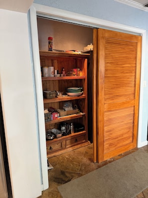 A wooden pantry with shelves, a coffee maker, and a kettle.