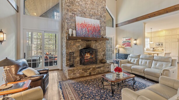 A spacious living room with a stone fireplace, leather sofas, a large rug, and a view of the outdoors. - 5-bedroom 3-Story Home w/ 3 Car Garage In Gated Community +Pool Table +Huge Deck (Highlands)