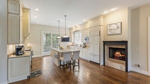 A spacious kitchen with a central island, white cabinetry, a fireplace, and a large window. - 5-bedroom 3-Story Home w/ 3 Car Garage In Gated Community +Pool Table +Huge Deck (Highlands)