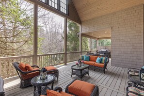 Eine überdachte Terrasse im Freien mit Korbmöbeln, einem Glastisch und einem Grill.