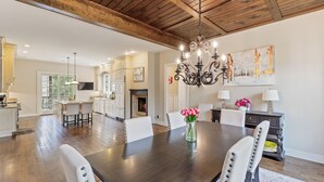 A spacious dining area with a dark wooden table, white chairs, a chandelier, and a painting on the wall. - 5-bedroom 3-Story Home w/ 3 Car Garage In Gated Community +Pool Table +Huge Deck (Highlands)