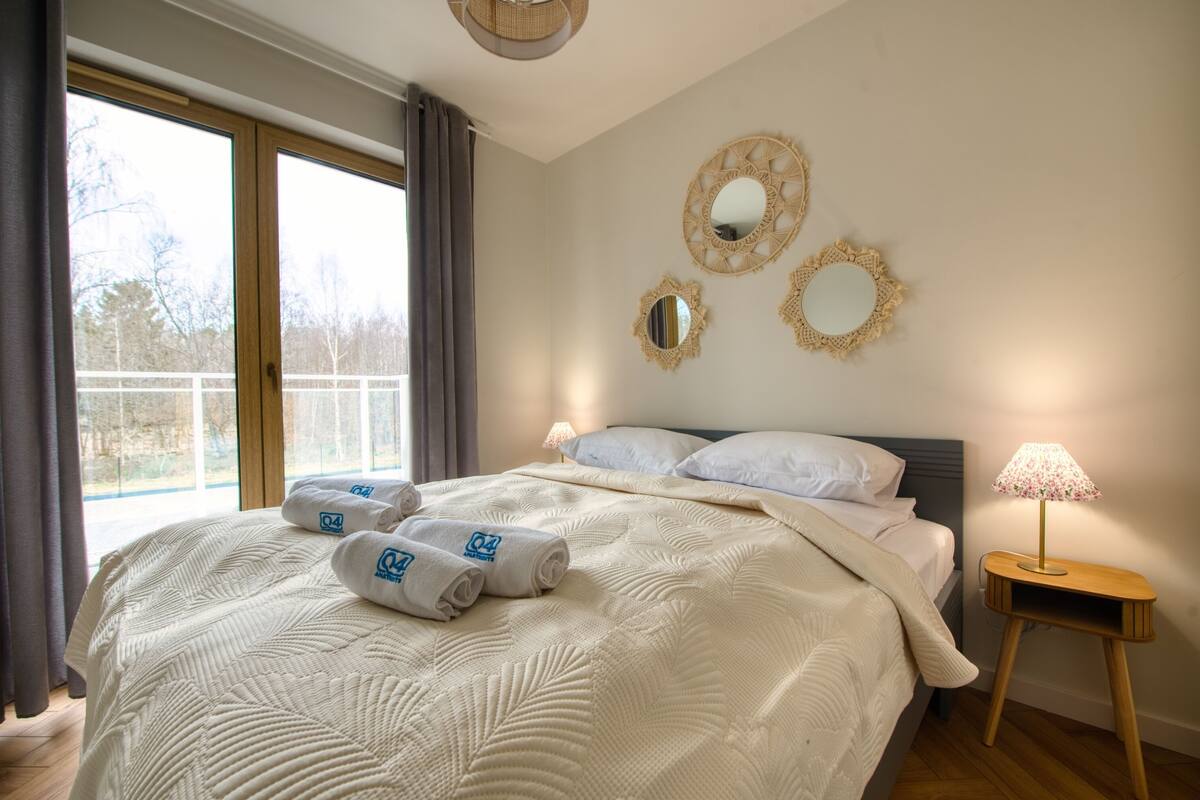 Ein Hotelzimmer mit einem großen Bett, zwei Wandspiegeln, einer Nachttischlampe und Balkonblick.