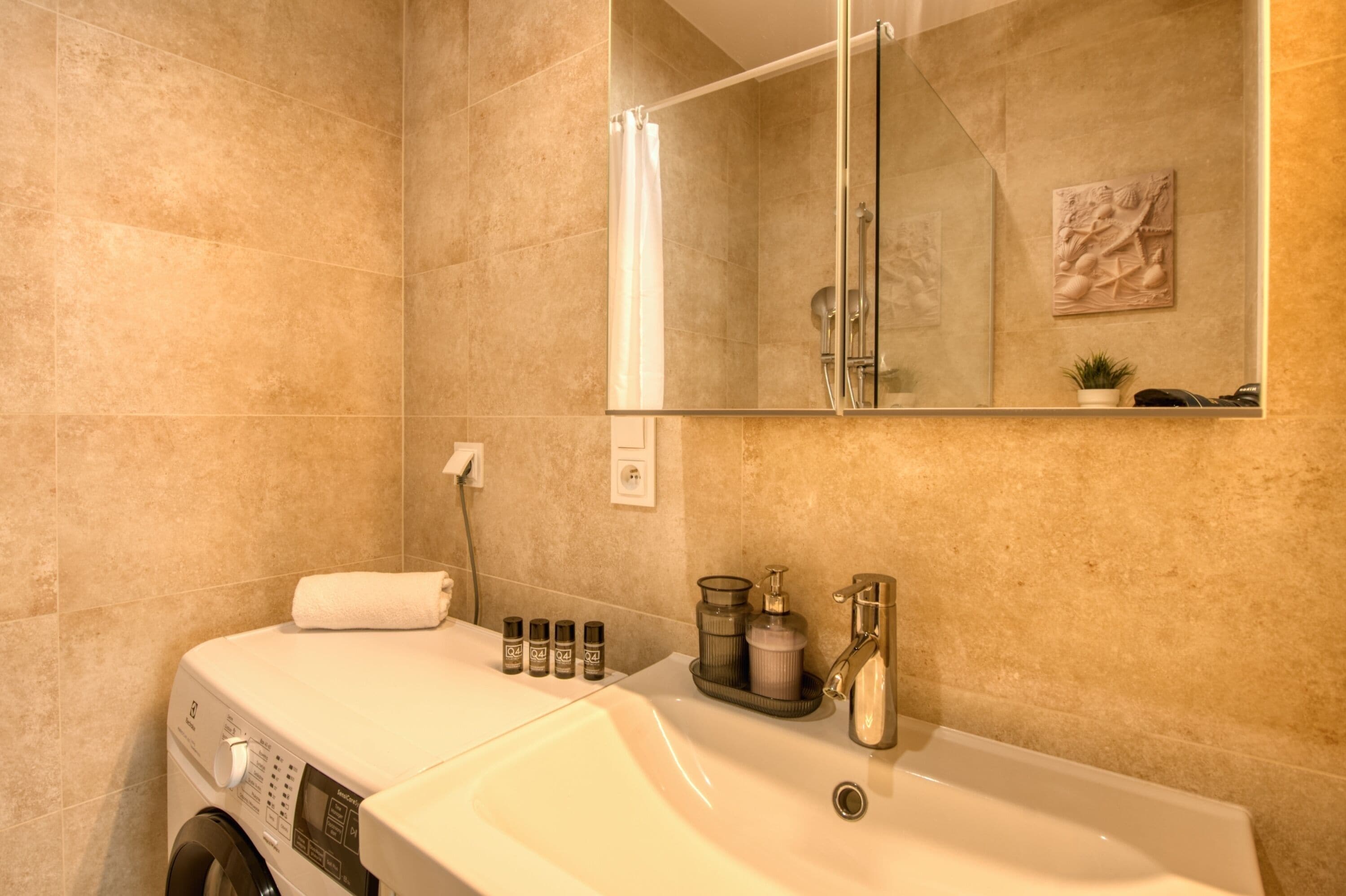 A bathroom with a washing machine, a sink, a mirror, and a shower.