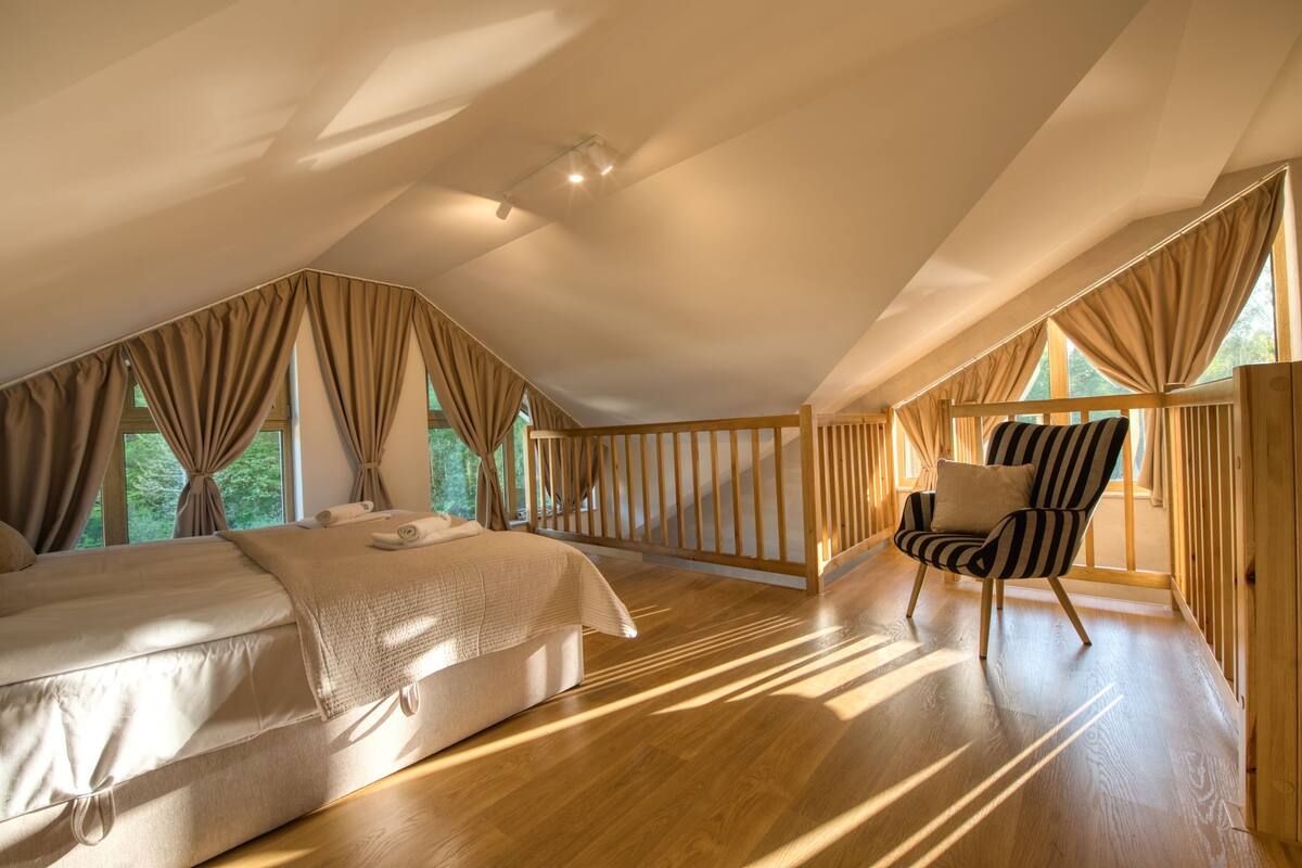 Ein Schlafzimmer mit einem großen Bett, einem Holzstuhl und Blick ins Freie.