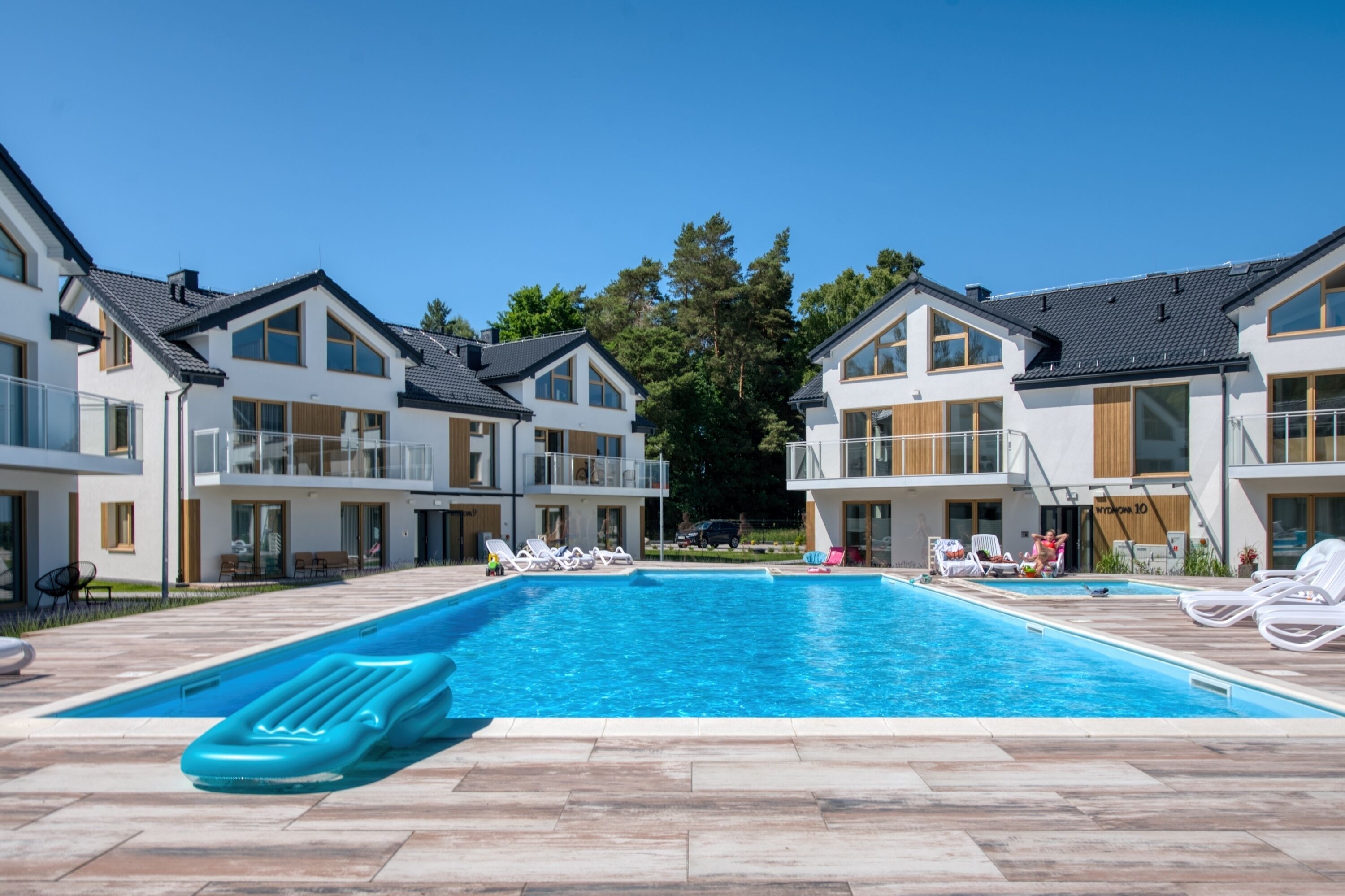 Un hotel moderno con piscina, sillones de descanso y un cielo azul despejado.