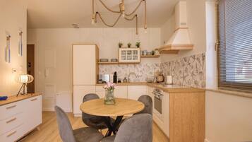 A modern kitchen with a round dining table, grey chairs, a hanging light fixture, and a built-in oven.