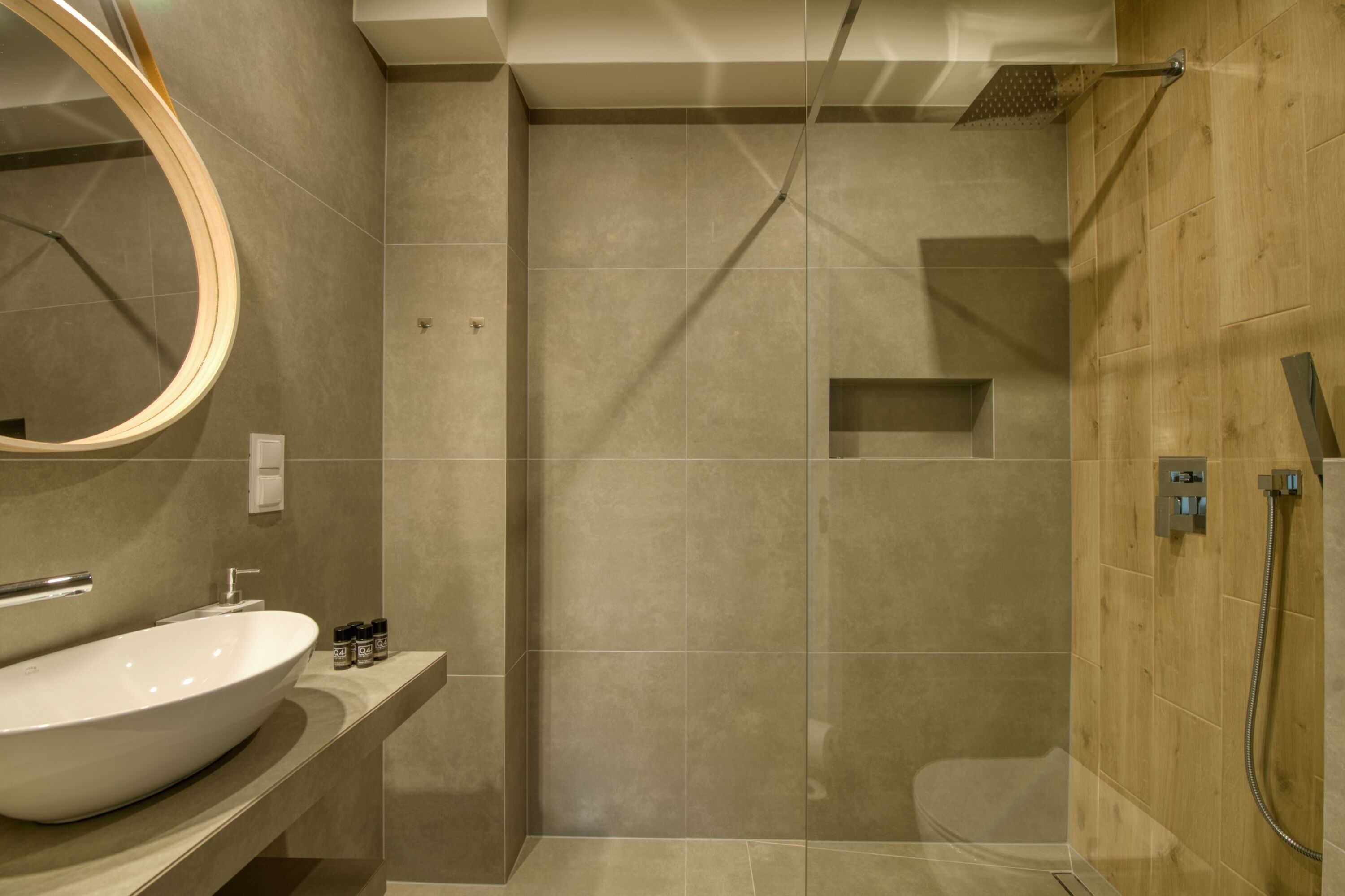 Un baño moderno con un lavamanos ovalado grande, un espejo, ducha con puerta de cristal y una pared de acento de madera.