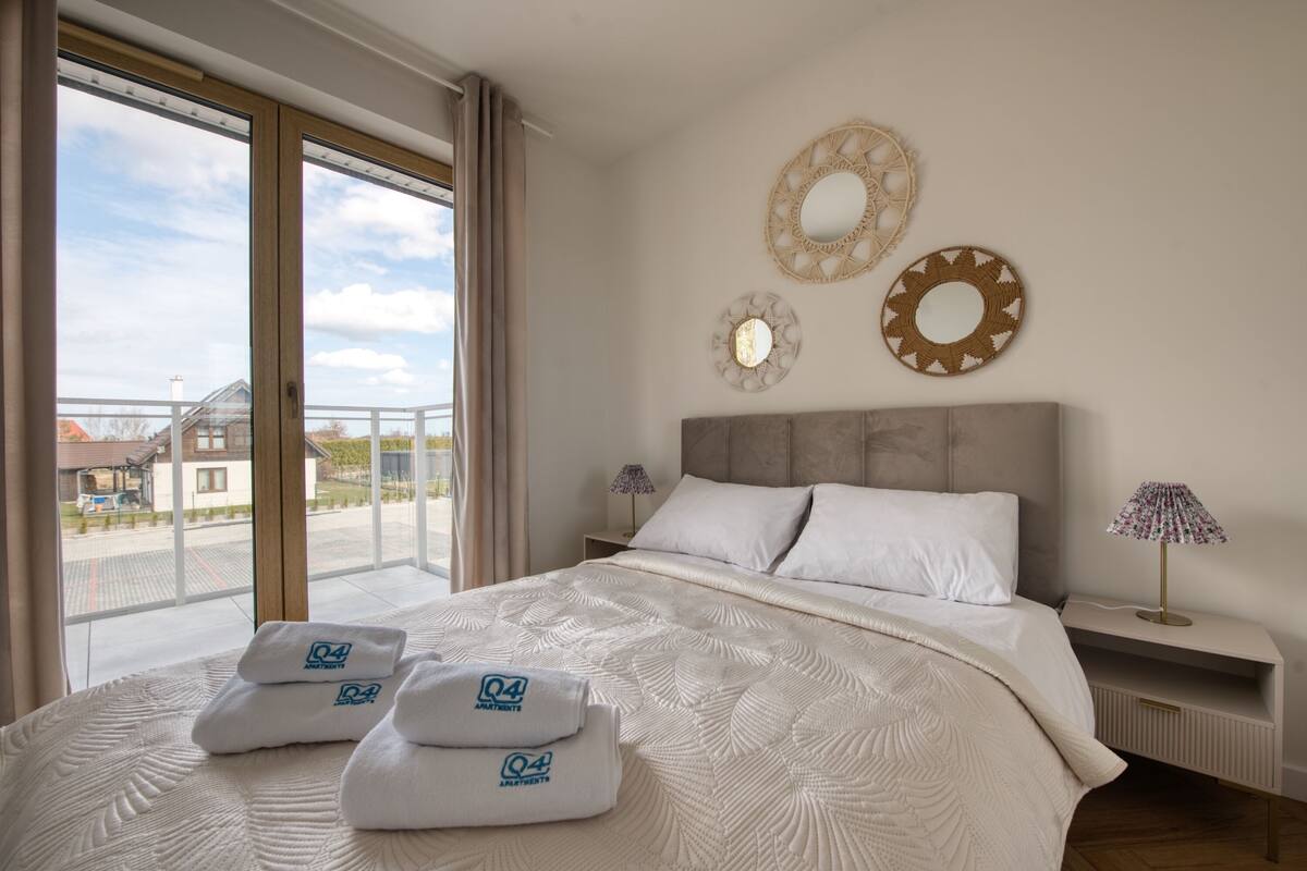 Ein Hotelzimmer mit einem großen Bett, zwei Wandspiegeln, einem Nachttisch mit Lampe und Blick ins Freie.