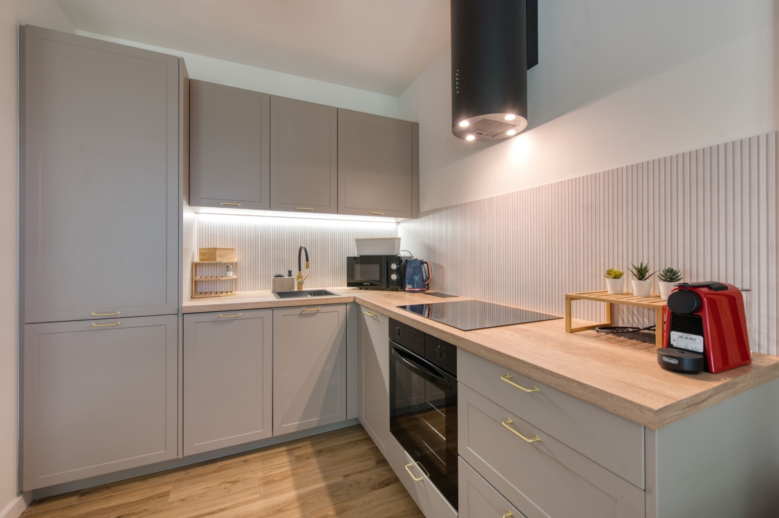 Una cocina moderna con armarios grises, encimera de madera, microondas y una cafetera roja.