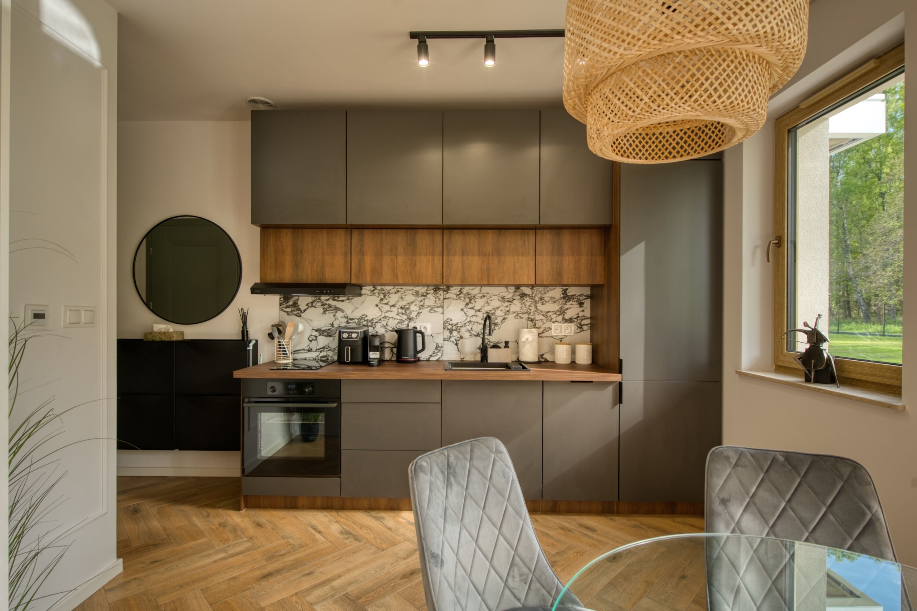 A modern kitchen with dark cabinets, a marble backsplash, and a dining area with a glass table and two chairs.