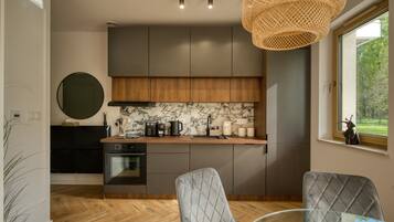 A modern kitchen with dark cabinets, a marble backsplash, and a dining area with a glass table and two chairs.
